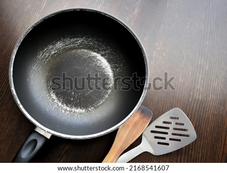 Old scratched non-stick pan on wood table. Teflon pan peeling off. Copy space is on the right side.  Royalty-Free Stock Photo #2168541607