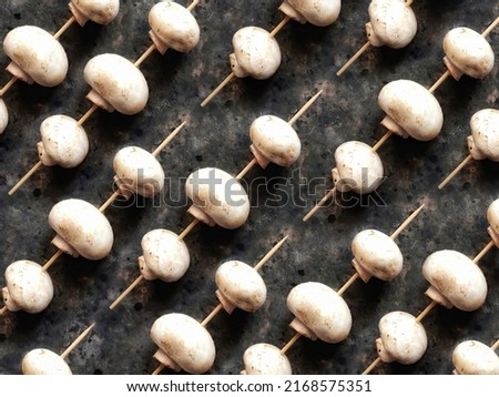 Background of champignons on a wooden skewer Mushroom pattern on a black concrete background. Vegetables to replace meat.