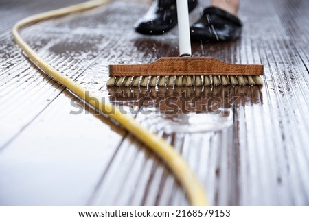 Detail of a man with a scrubbing brush and a water hose making spring cleaning on a wooden terrace Royalty-Free Stock Photo #2168579153