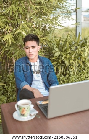 A handsome asian male freelancer with his laptop and a cup of coffee at an al fresco outdoor cafe. Modern young professional working remotely. Royalty-Free Stock Photo #2168586551