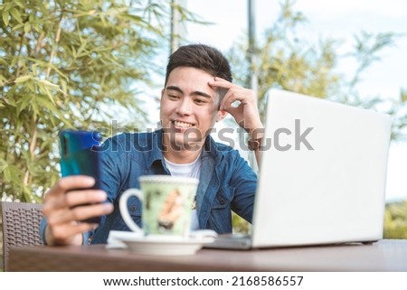 A handsome man with amblyopia browsing his social media or chatting with someone on his cellphone. Taking a break after some remote work at an outdoor al fresco cafe. Royalty-Free Stock Photo #2168586557