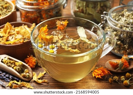 Freshly brewed tea and dried herbs on wooden table, closeup