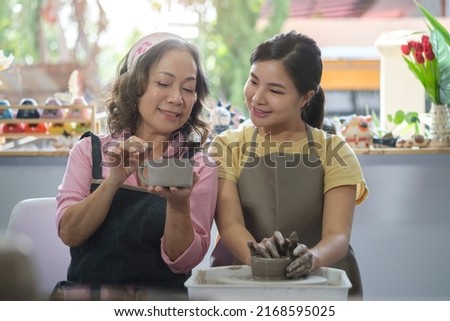 Mature woman and young craftswoman working on pottery wheel together in handmade ceramics workshop.