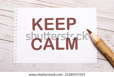On a light wooden background, a colored pencil and a white sheet of paper with the text KEEP CALM