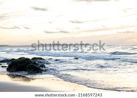 Beautiful waves with white foam crashing on the big rocks at the shore of Cap Blanc-Nez, France with a beautiful dramatic sunset in the background. High quality photo