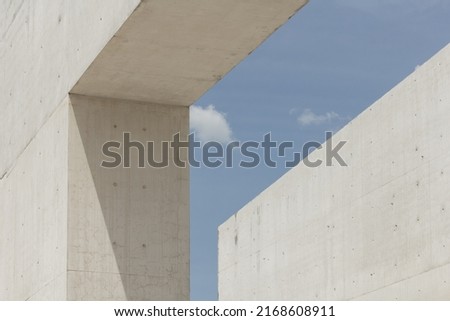Architectural photography. Geometric composition with two large and strong cement blocks. building against the blue sky with white clouds. Modern structures architecture. Minimalist design fragments. Royalty-Free Stock Photo #2168608911