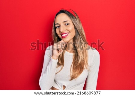 Beautiful hispanic woman wearing red diadem looking confident at the camera with smile with crossed arms and hand raised on chin. thinking positive. 