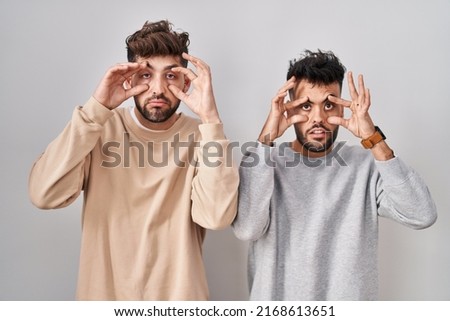 Young homosexual couple standing over white background trying to open eyes with fingers, sleepy and tired for morning fatigue 