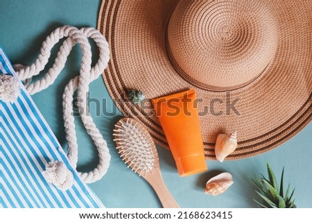 Flat lay summer travel photography. Striped bag, straw hat, orange sunscreen tube, wooden hair brush and seashells. Beach essentials, vacation packing