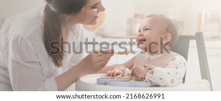 Mother feeding her cute little baby in kitchen. Banner design Royalty-Free Stock Photo #2168626991