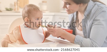 Mother feeding her cute little baby in kitchen. Banner design Royalty-Free Stock Photo #2168627041