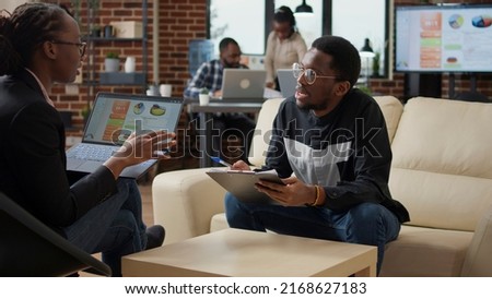 Woman explaining data charts on laptop and man taking notes on documents, doing job collaboration to create financial analysis strategy. Business people working together to plan project.