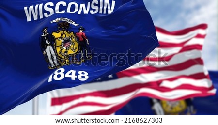 The Wisconsin state flag waving along with the national flag of the United States of America. Wisconsin is a state in the upper Midwestern United States Royalty-Free Stock Photo #2168627303