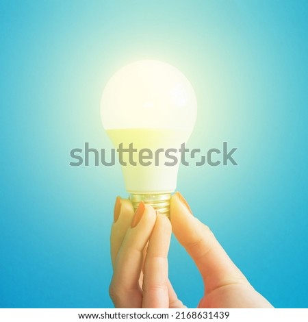 lamp in a woman's hand. female fingers holding LED lamp. idea. New idea or inspiration concept. Concept of startup. blue background. Square image.