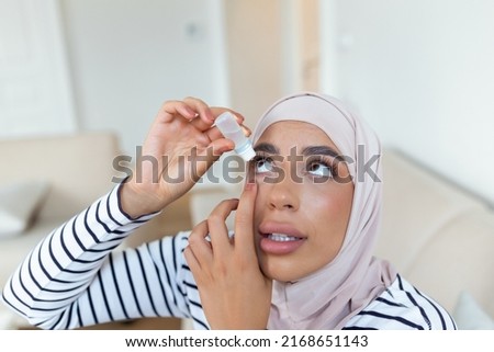 Arabic woman with hijab using eye drop, dropping eye lubricant to treat dry eye or allergy, sick woman treating eyeball irritation or inflammation woman suffering from irritated eye, optical symptoms