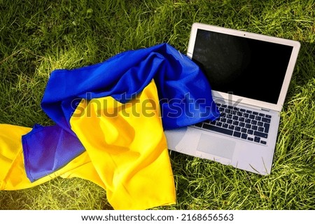 Laptop computer and flag of Ukraine on the grass in the park.