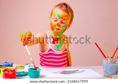 Little cute girl with children's colorful makeup painted hands painting the picture. Education, leisure, happy childhood and art concept. Horizontal image.