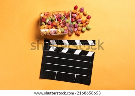 Photo of movie clapper and colored pop corn on yellow background