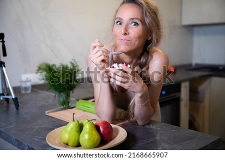 A young beautiful blonde with blue eyes of Caucasian appearance eats with great appetite fresh healthy food at the kitchen table at home. On the face of the girl the emotion of pleasure and fun. next Royalty-Free Stock Photo #2168665907