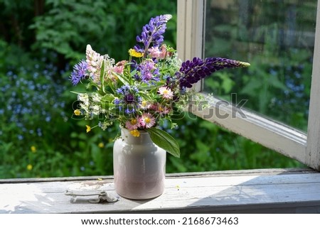 Bouquet of wild flowers in a vase on a wooden window sill. Still life on the window of an old country house, summer cottage. Floral home decoration.  Royalty-Free Stock Photo #2168673463