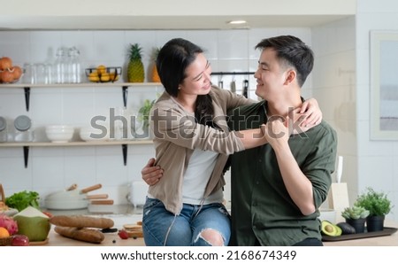 Portrait of young Asian couple standing in the kitchen, happy romantic lover smiling and looking at each other, beautiful woman and handsome man hugging while cooking together at home