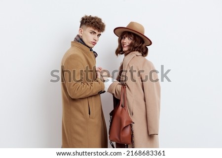 a beautiful, pleasant couple, a man and a woman are standing on a light background holding hands, dressed in warm brown autumn coats. Horizontal Studio Photography