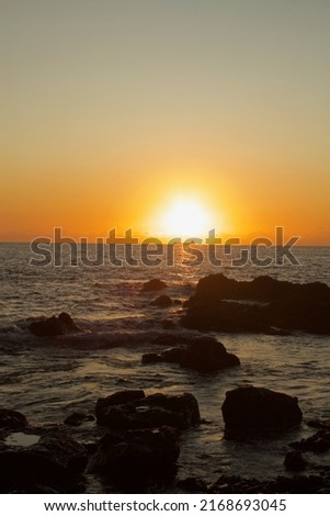 picture taken from the beach during sunset with lava rocks in the foreground