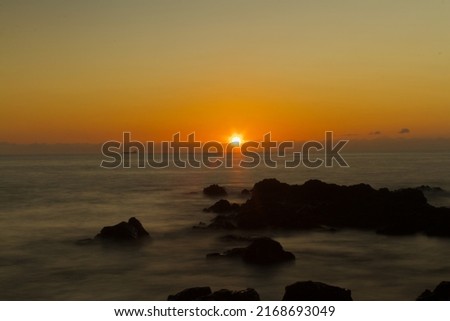Long exposure picture taken from the beach during sunset with volcanic rocks in the foreground