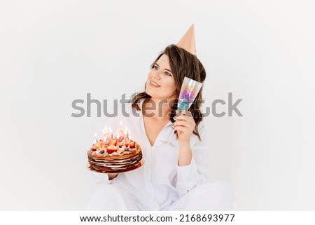 a happy woman with champagne and a birthday cake with candles. traditional sweet treat and wish-making for a birthday.