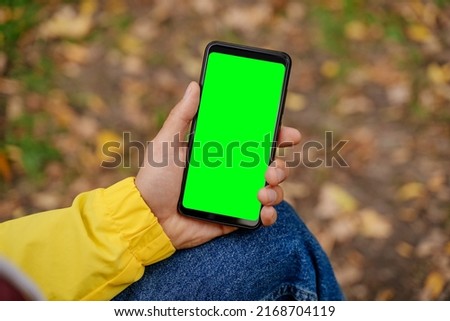 A man in a yellow jacket holds a smartphone with a green screen in his hand. Autumn Day