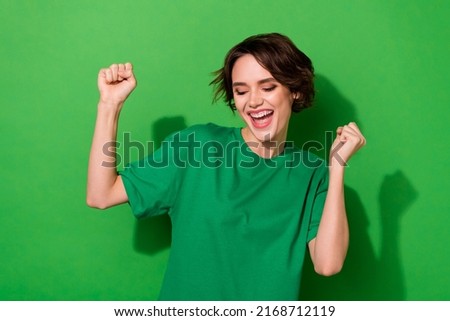 Photo of lucky funny young lady dressed casual t-shirt smiling rising fists isolated green color background Royalty-Free Stock Photo #2168712119