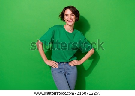 Photo of funky charming woman wear casual t-shirt hands arms waist smiling isolated green color background