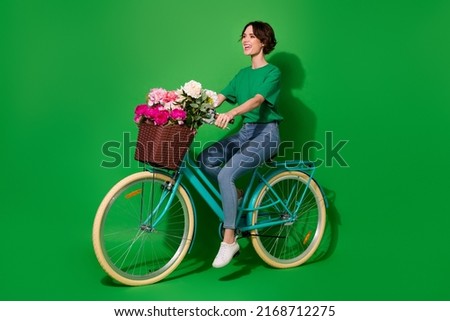 Full body profile photo of stunning cheerful lady ride bike look empty space isolated on green color background Royalty-Free Stock Photo #2168712275
