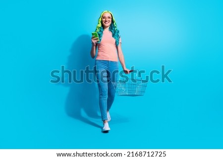 Full size photo of young charming woman go on shopping buy groceries hold smartphone isolated on blue color background