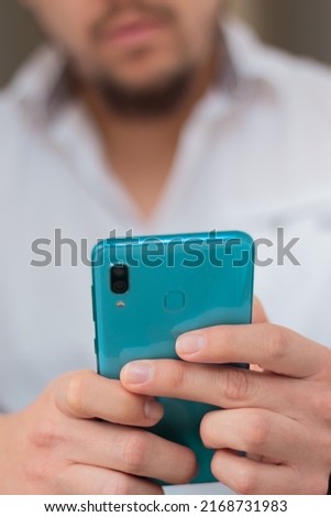 Unrecognizable man with unfocused face holding cyan cell phone