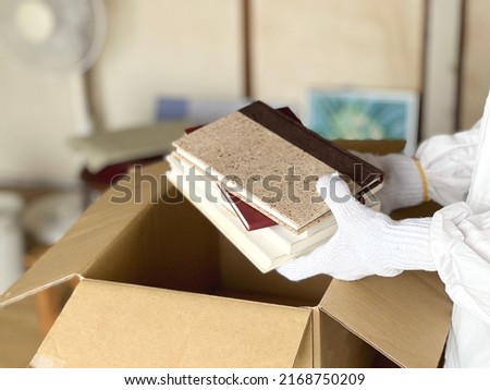 A messy room with a hand that puts books etc. in a cardboard box Royalty-Free Stock Photo #2168750209
