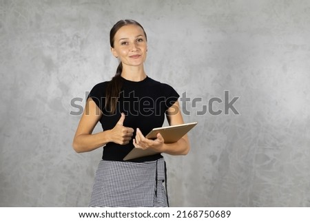portrait of happy smiling pretty woman shows thumb up, looks at camera and use tablet with copy space at background. pretty caucasian woman relax working business at home office
