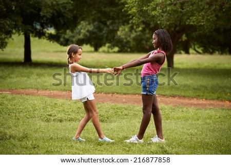 Two hispanic and african little girls playing ring around the rosie in public park and holding hands Royalty-Free Stock Photo #216877858