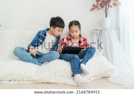 Portrait boy and girl sitting on the soda in the living room isolate on white background. Girl playing game in tablet and boy looking at tablet.  Feeling happy. Technology and learning concept