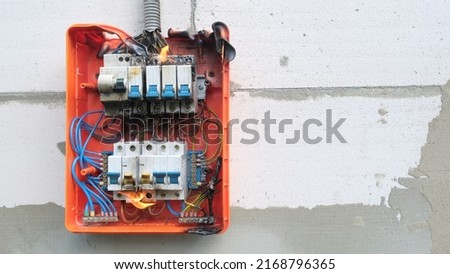 Burning switchboard from overload or short circuit on wall. Circuit breakers on fire and smoke from overheating due to poor connection. Dangerous home electrical wiring concept, copy space Royalty-Free Stock Photo #2168796365