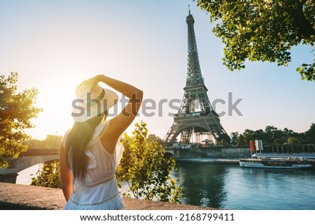 Young woman tourist in sun hat and white dress standing in front of Eiffel Tower in Paris at sunset. Travel in France, tourism concept Royalty-Free Stock Photo #2168799411