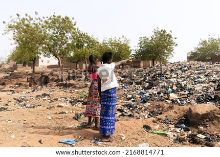 Two African girls pointing to the mountain of garbage that occupies the street of their village indicating the mismanagement of waste that afflicts their continent Royalty-Free Stock Photo #2168814771