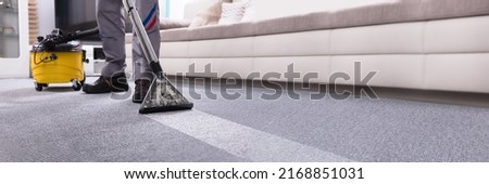Low Section Of A Person Cleaning The Carpet With Vacuum Cleaner In Living Room