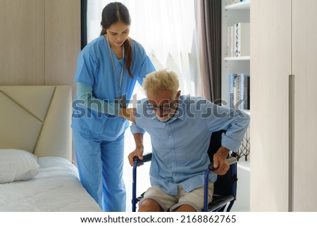 Asian smiling nurse helping senior man get out of bed nursing care support patient while getting out of bed and moving to wheelchair at home helping handicapped elderly stand up