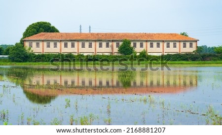Isolated farm in the green countryside outside Milan, Lombardy, Italy.  The farm is reflecting in the paddy field full of water, dedicated to the cultivation of rice. Royalty-Free Stock Photo #2168881207