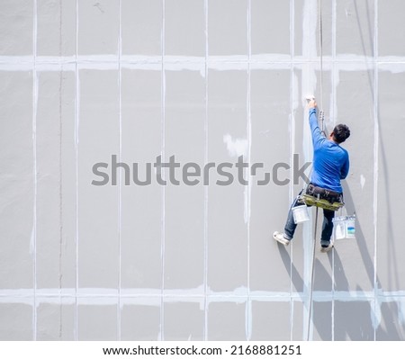 Male painter is using rappelling rope to paint tall buildings, specialized work where danger and accident prone, safety protection is not up to standard. Royalty-Free Stock Photo #2168881251