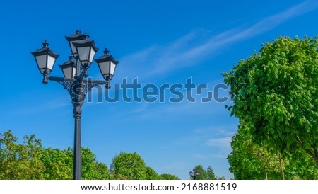 Vintage street lamp on blue sky and green trees background. Close-up. Old-fashioned lampost. Space for text. Nature background.