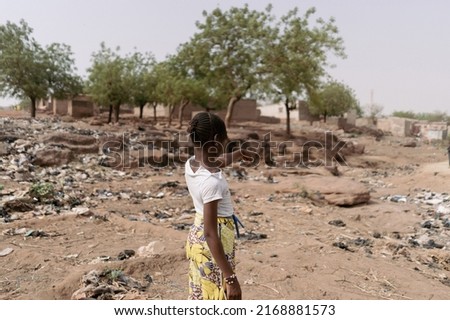 Young african girl standing with her back to the camera pointing to the desolate landscape of her homeland characterized by climate change, desertification and waste pollution Royalty-Free Stock Photo #2168881573