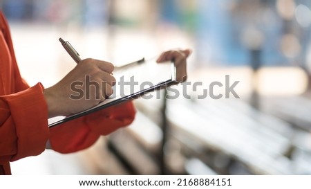 Action of safety officer is writing on safety checklist document during safety audit and inspection, with factory workshop as blurred background. Industrial expertise occupation photo. Selective focus Royalty-Free Stock Photo #2168884151
