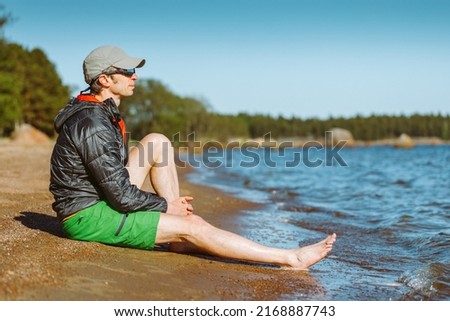 A man sits on a summer beach and contemplates a beautiful seascape. Man in focus background is blurred.